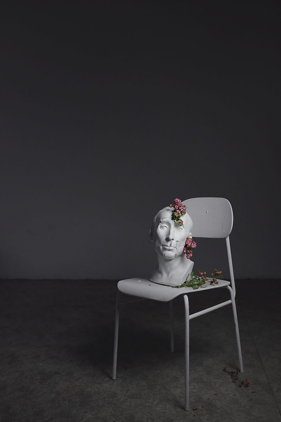 White sculpture of a male head with flowers on a white chair