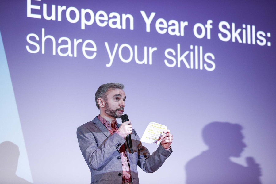 Man on the stage, European Year of Skills: share your skills visual at the background