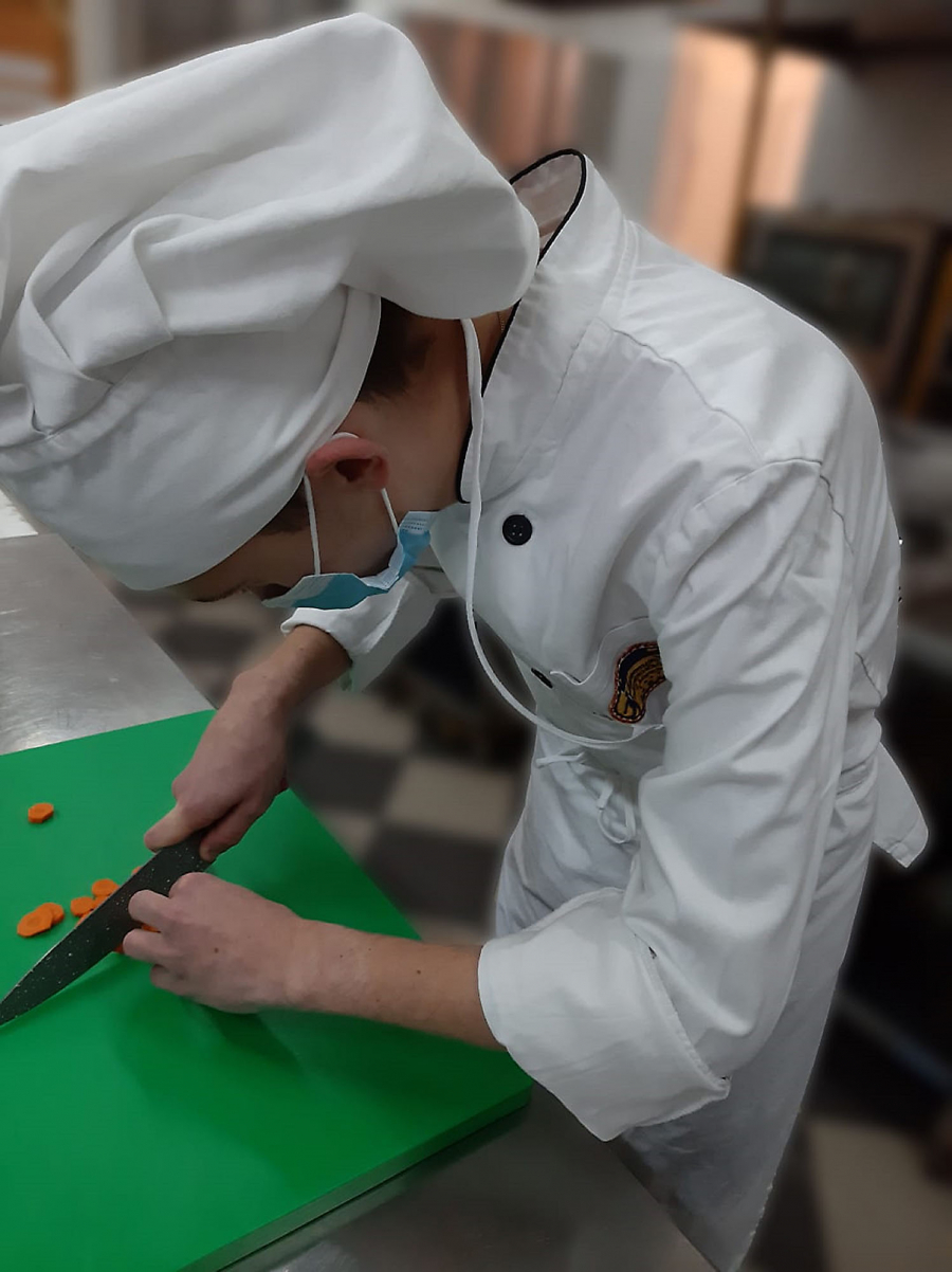Young male chef chopping carrots